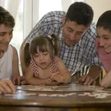 Une famille joue à un puzzle. La petite fille, atteinte de trisomie 21, est au centre de l'attention.