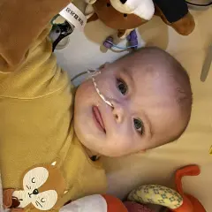Un bébé avec une sonde nasogastrique, entouré de peluches. L'espoir d'une vie longue malgré la maladie de Pompe.