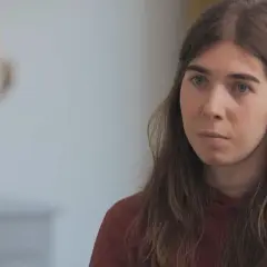 Une jeune femme aux cheveux longs et châtains, portant un sweat à capuche bordeaux, écoute attentivement une personne dont on ne voit que le dos. Elle semble réfléchir à son parcours pour changer de sexe.
