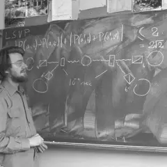Un homme devant un tableau noir, expliquant des formules complexes, peut-être sur les inégalités de Bell.