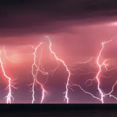Un ciel orageux aux teintes roses et violettes, illuminé par un **éclair de chaleur** spectaculaire qui déchire l'horizon au-dessus de la mer.