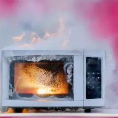 Un micro-ondes en feu, dégageant une épaisse fumée blanche et des flammes orangées. Un véritable danger micro onde.