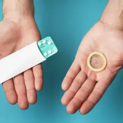 Deux mains ouvertes présentent une plaquette de pilules contraceptives et un préservatif, symbolisant les options de contraception hormonale masculine.