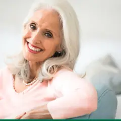 Une femme souriante aux cheveux argentés, portant un collier de perles. Elle rayonne de beauté, prouvant qu'il n'y a pas d'âge précis pour savoir à quel âge une femme vieillit.