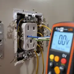 Un multimètre affiche 00V, une unité de mesure de la tension, près d'une prise électrique en cours d'installation.