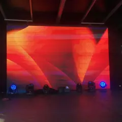 Écran LED géant diffusant un motif abstrait rouge et orange, créant un effet de moiré visuellement captivant. Des projecteurs bleus et noirs sont disposés au sol.