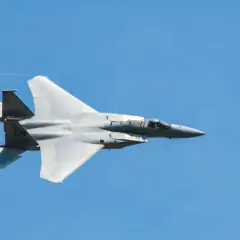 Un avion de chasse gris fend le ciel bleu, laissant une traînée de condensation. Sa silhouette élancée suggère une vitesse impressionnante.