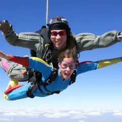 Deux personnes en tandem profitent de la vitesse d'un saut en parachute, bras écartés, au-dessus des nuages.