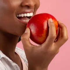 Une femme souriante tient une pomme rouge, un coupe faim naturel parfait pour une pause saine.