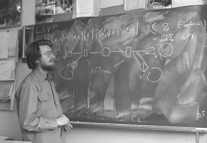 Un homme devant un tableau noir, expliquant des formules complexes, peut-être sur les inégalités de Bell.
