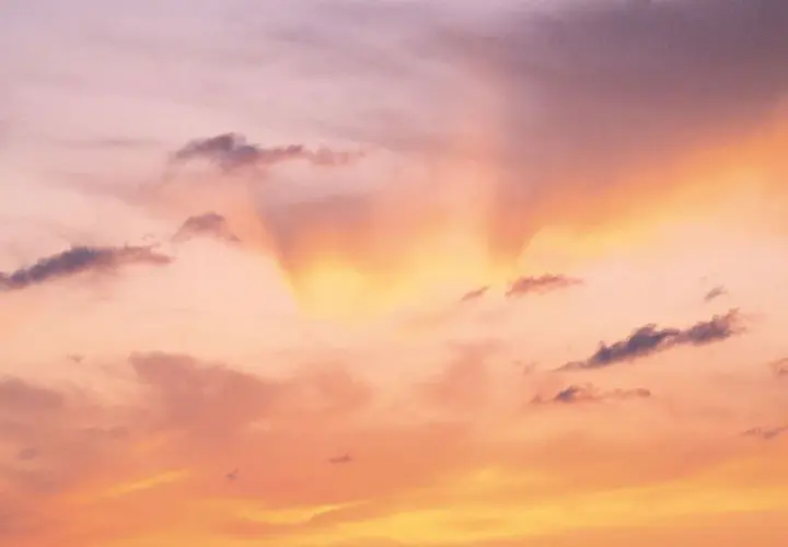 Le ciel est rose, teinté d'orange et de jaune, avec des nuages sombres. Une douce lumière filtre, expliquant pourquoi le ciel est rose.