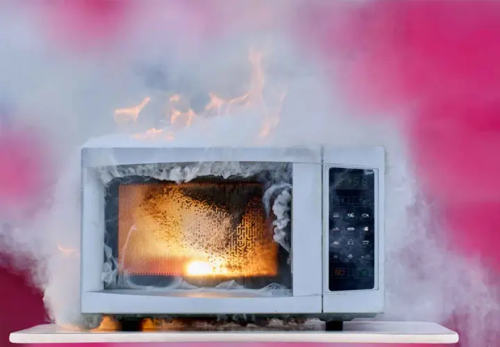 Un micro-ondes en feu, dégageant une épaisse fumée blanche et des flammes orangées. Un véritable danger micro onde.