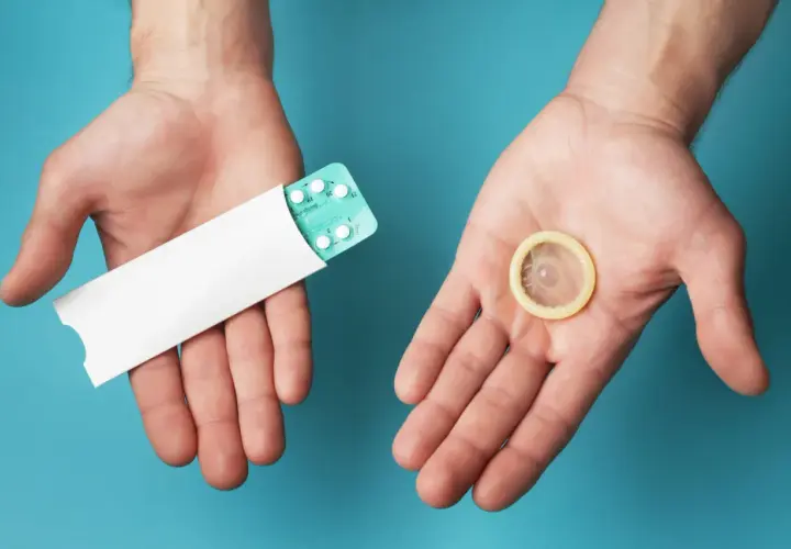 Deux mains ouvertes présentent une plaquette de pilules contraceptives et un préservatif, symbolisant les options de contraception hormonale masculine.