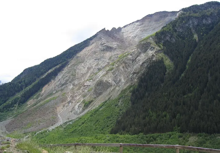 Vaste glissement de terrain suisse, une montagne dénudée de roche et de terre, contrastant avec une forêt dense.