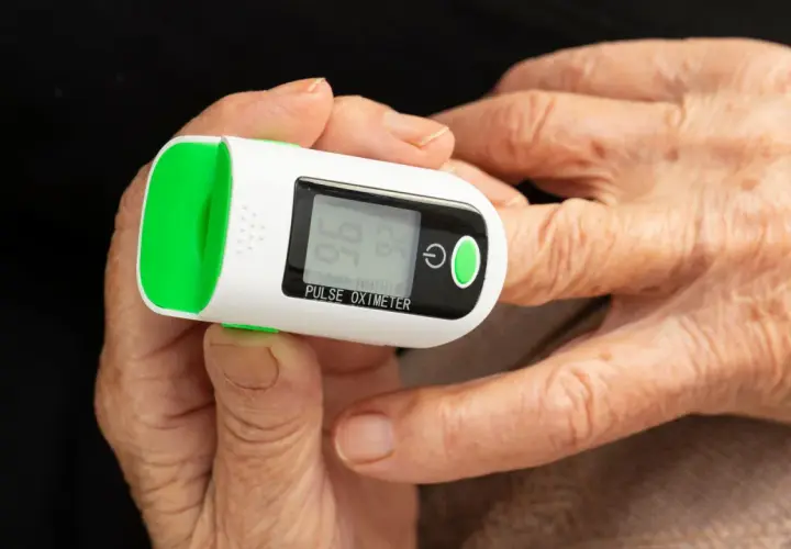 Doigt âgé sur oxymètre mesurant le taux d'oxygène dans le sang. Affichage de 96% SpO2 et 74 bpm.