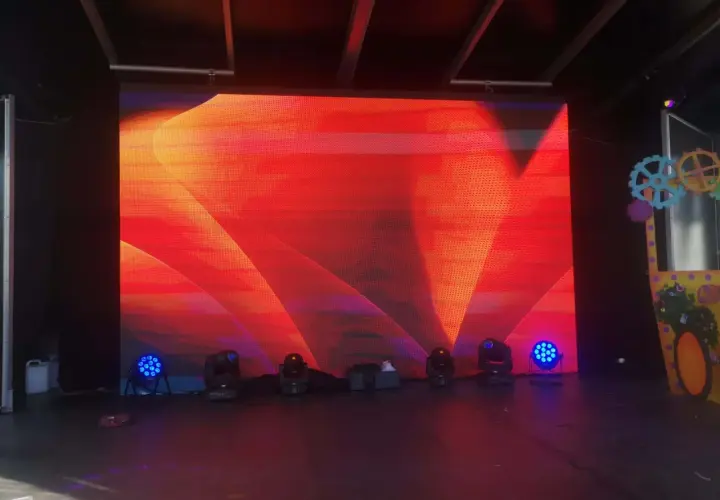 Écran LED géant diffusant un motif abstrait rouge et orange, créant un effet de moiré visuellement captivant. Des projecteurs bleus et noirs sont disposés au sol.