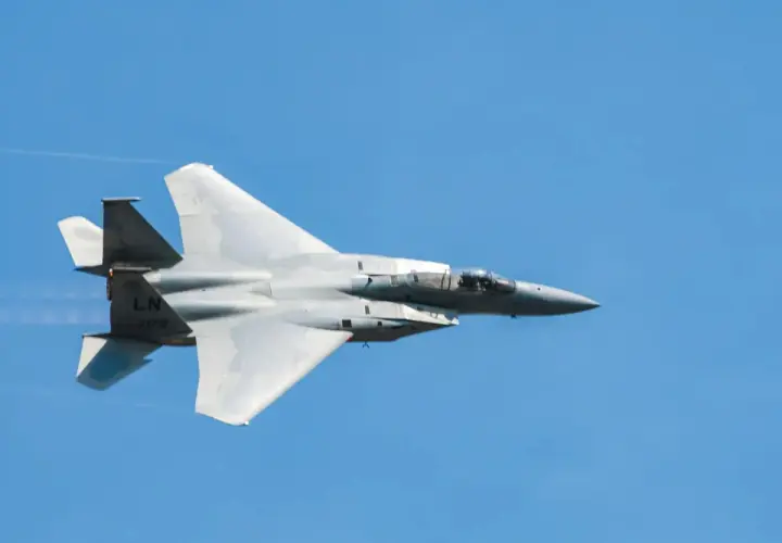 Un avion de chasse gris fend le ciel bleu, laissant une traînée de condensation. Sa silhouette élancée suggère une vitesse impressionnante.