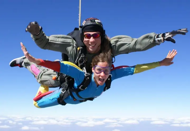 Deux personnes en tandem profitent de la vitesse d'un saut en parachute, bras écartés, au-dessus des nuages.