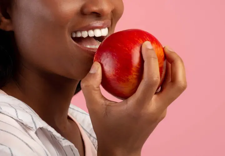 Une femme souriante tient une pomme rouge, un coupe faim naturel parfait pour une pause saine.