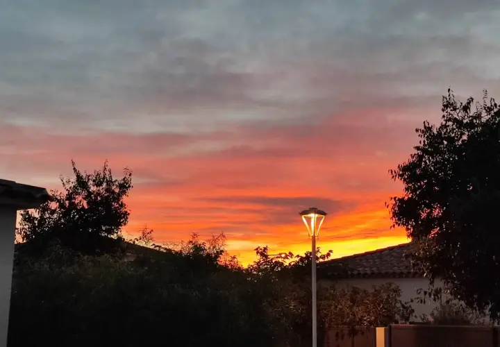 Ciel embrasé par un coucher de soleil couleur orange et rose, avec des nuages gris. Un lampadaire éclaire la scène.