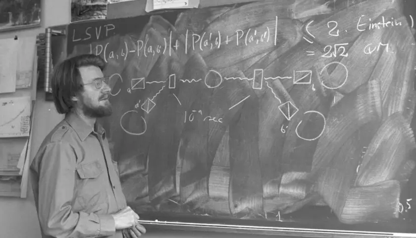Un homme devant un tableau noir, expliquant des formules complexes, peut-être sur les inégalités de Bell.