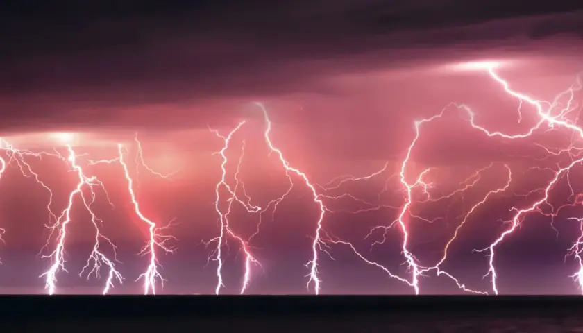 Un ciel orageux aux teintes roses et violettes, illuminé par un **éclair de chaleur** spectaculaire qui déchire l'horizon au-dessus de la mer.