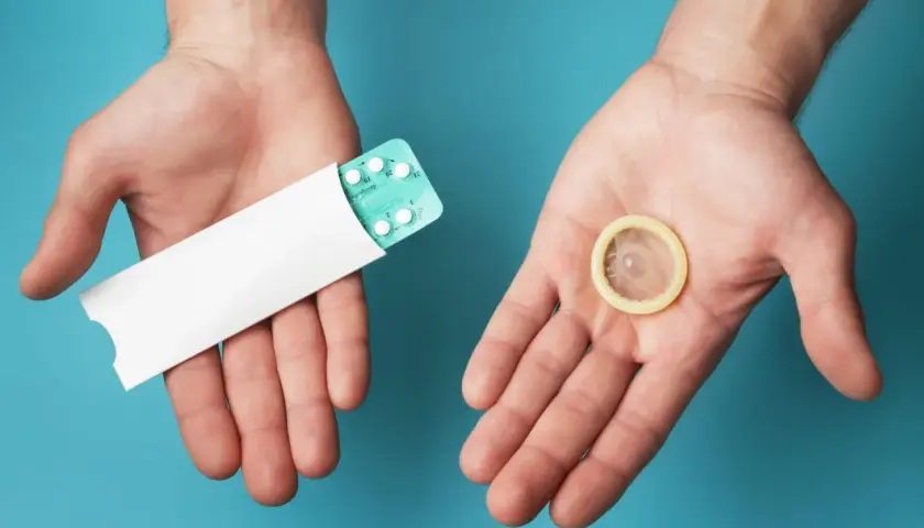 Deux mains ouvertes présentent une plaquette de pilules contraceptives et un préservatif, symbolisant les options de contraception hormonale masculine.