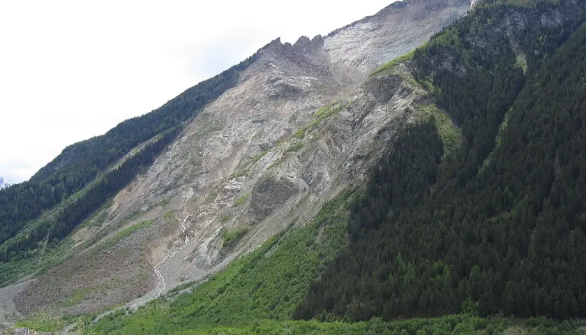 Vaste glissement de terrain suisse, une montagne dénudée de roche et de terre, contrastant avec une forêt dense.