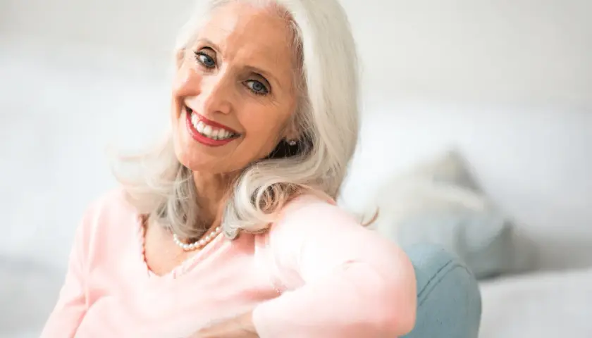 Une femme souriante aux cheveux argentés, portant un collier de perles. Elle rayonne de beauté, prouvant qu'il n'y a pas d'âge précis pour savoir à quel âge une femme vieillit.