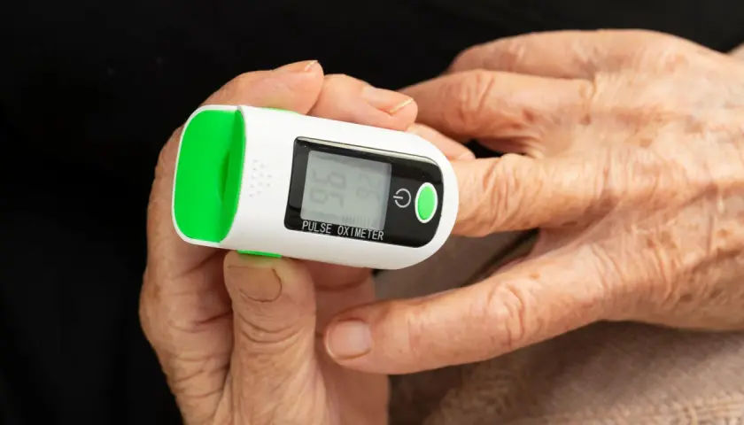 Doigt âgé sur oxymètre mesurant le taux d'oxygène dans le sang. Affichage de 96% SpO2 et 74 bpm.