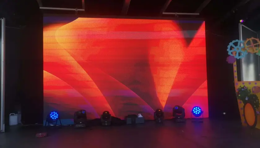 Écran LED géant diffusant un motif abstrait rouge et orange, créant un effet de moiré visuellement captivant. Des projecteurs bleus et noirs sont disposés au sol.