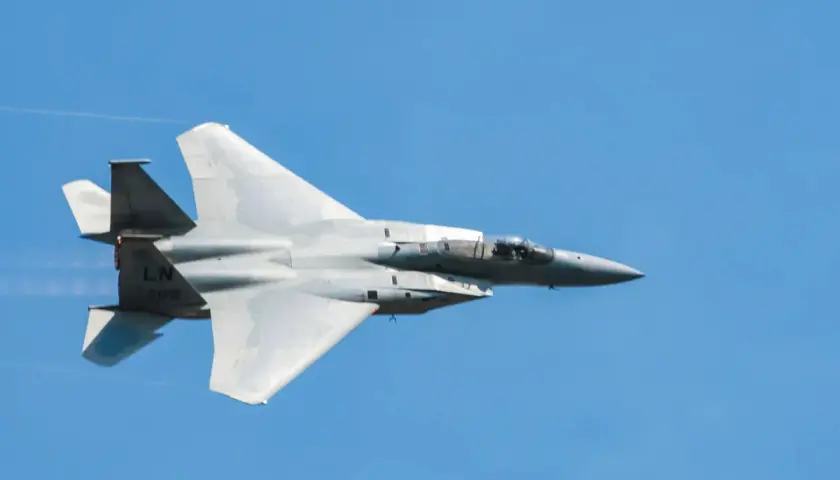 Un avion de chasse gris fend le ciel bleu, laissant une traînée de condensation. Sa silhouette élancée suggère une vitesse impressionnante.