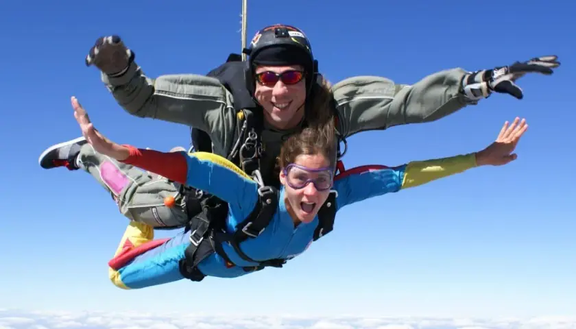 Deux personnes en tandem profitent de la vitesse d'un saut en parachute, bras écartés, au-dessus des nuages.