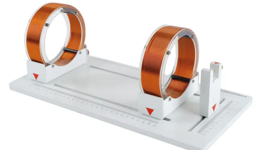 Deux bobines de Helmholtz en cuivre sur un support blanc avec une règle graduée.