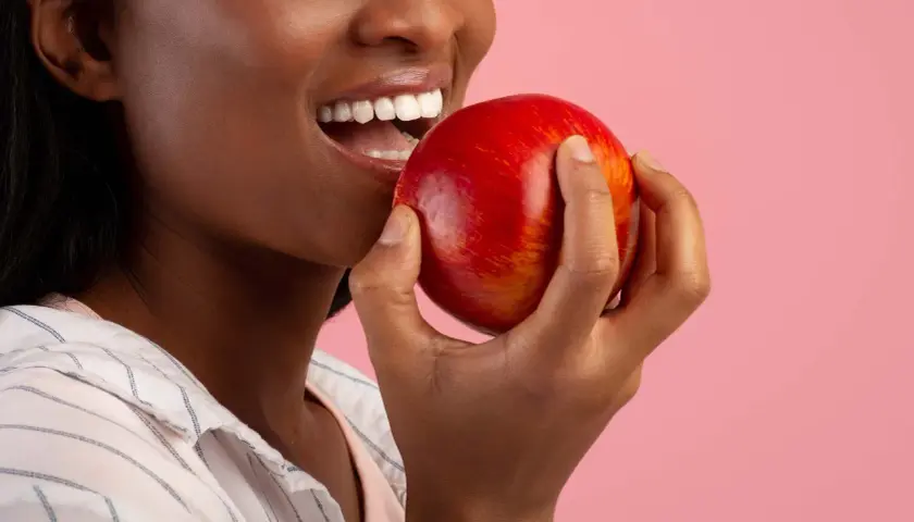 Une femme souriante tient une pomme rouge, un coupe faim naturel parfait pour une pause saine.