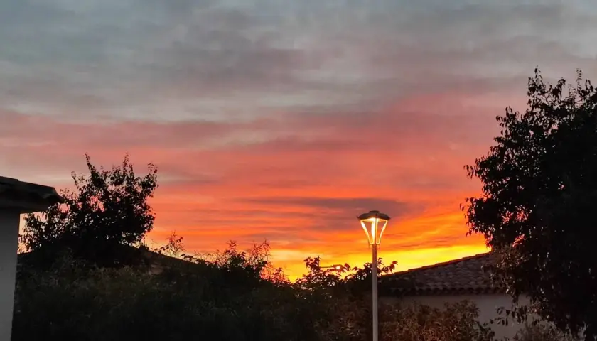 Ciel embrasé par un coucher de soleil couleur orange et rose, avec des nuages gris. Un lampadaire éclaire la scène.