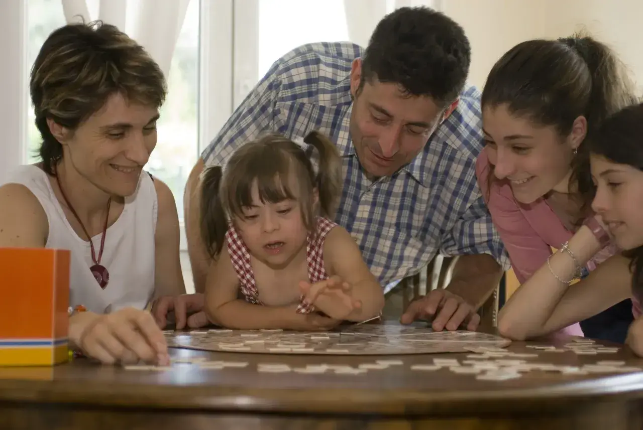 Une famille joue à un puzzle. La petite fille, atteinte de trisomie 21, est au centre de l'attention.