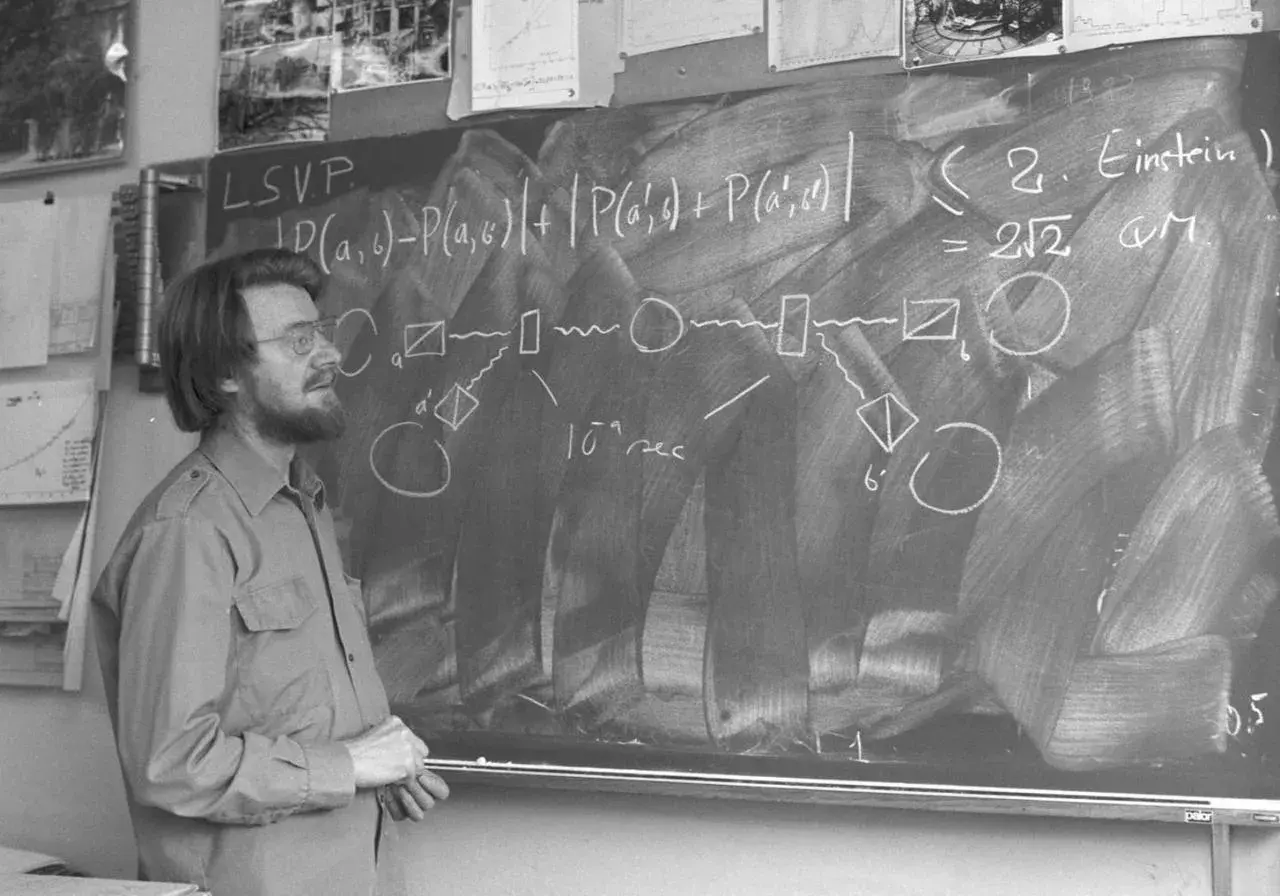 Un homme devant un tableau noir, expliquant des formules complexes, peut-être sur les inégalités de Bell.