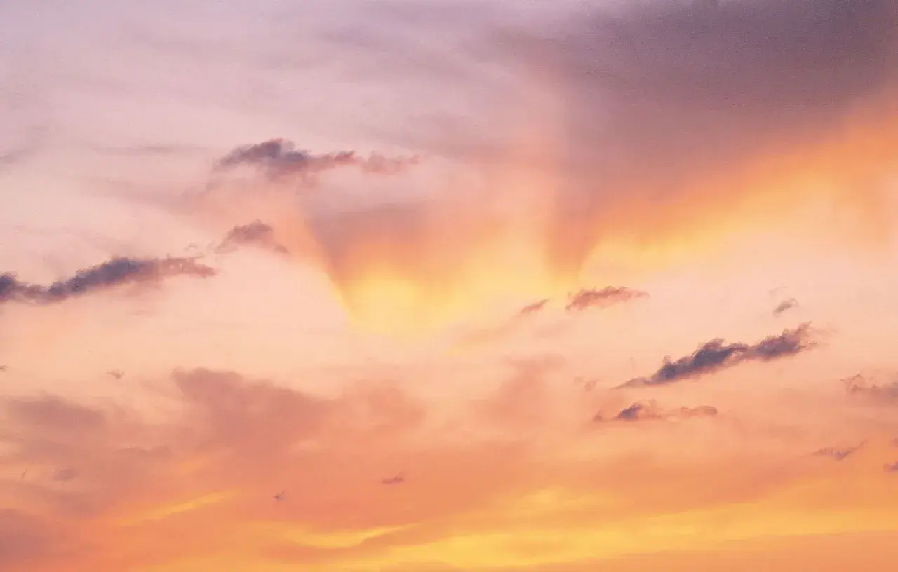 Le ciel est rose, teinté d'orange et de jaune, avec des nuages sombres. Une douce lumière filtre, expliquant pourquoi le ciel est rose.
