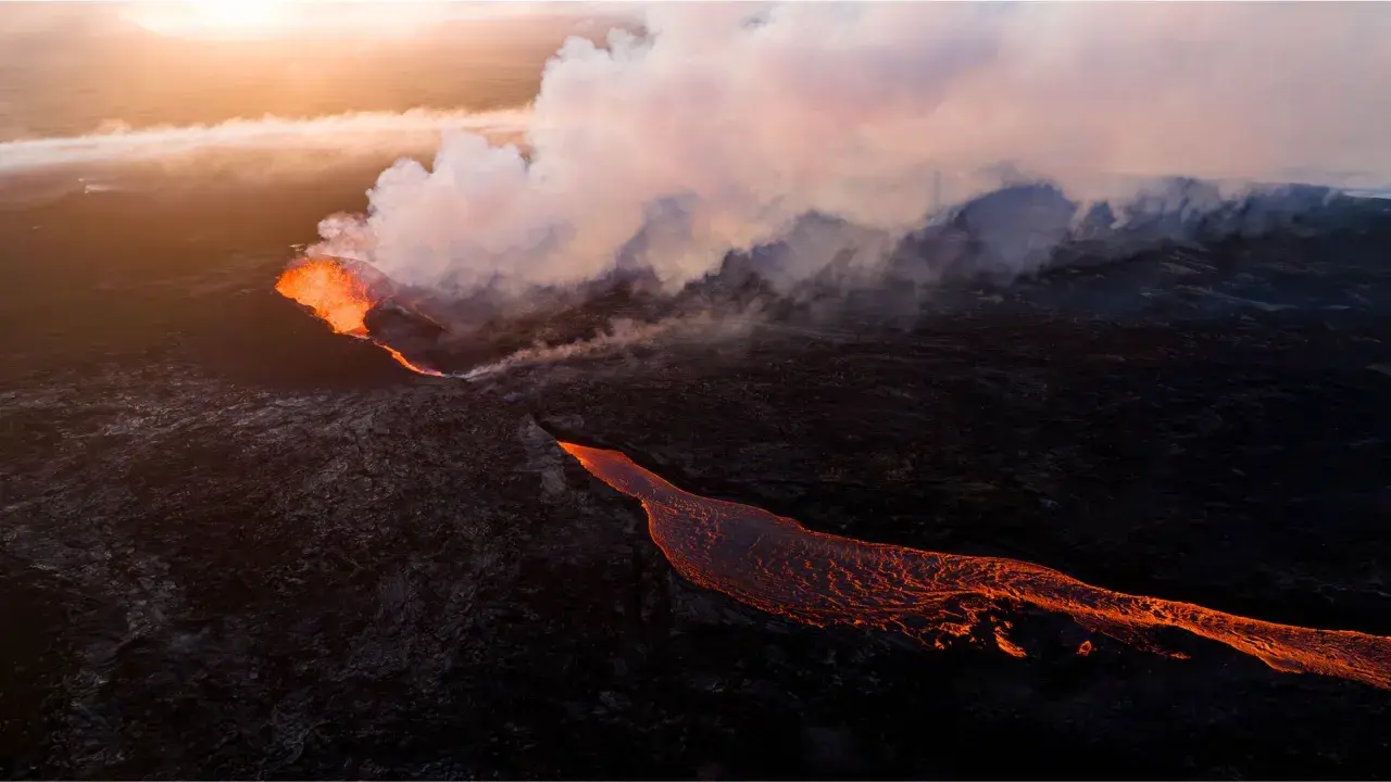 Éruption volcanique en Islande : la lave incandescente coule sur le paysage sombre, baignée par la lumière dorée du soleil couchant.