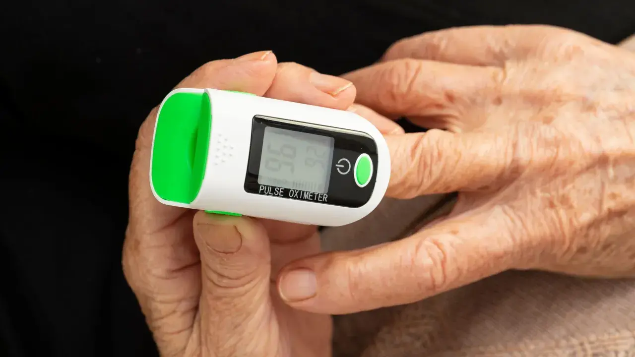 Doigt âgé sur oxymètre mesurant le taux d'oxygène dans le sang. Affichage de 96% SpO2 et 74 bpm.