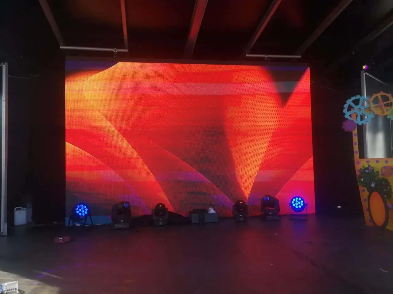 Écran LED géant diffusant un motif abstrait rouge et orange, créant un effet de moiré visuellement captivant. Des projecteurs bleus et noirs sont disposés au sol.