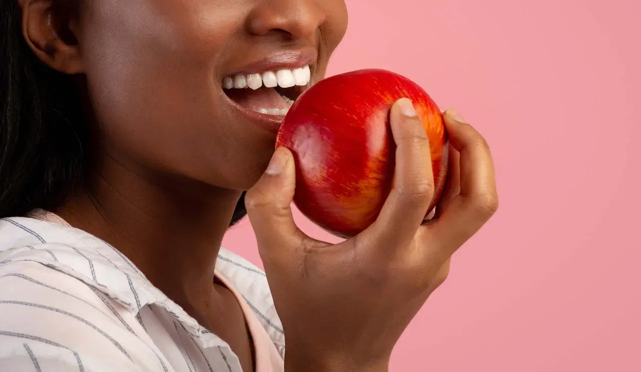 Une femme souriante tient une pomme rouge, un coupe faim naturel parfait pour une pause saine.