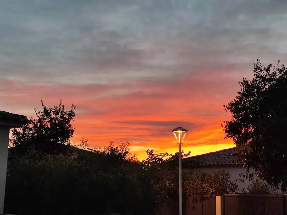 Ciel embrasé par un coucher de soleil couleur orange et rose, avec des nuages gris. Un lampadaire éclaire la scène.