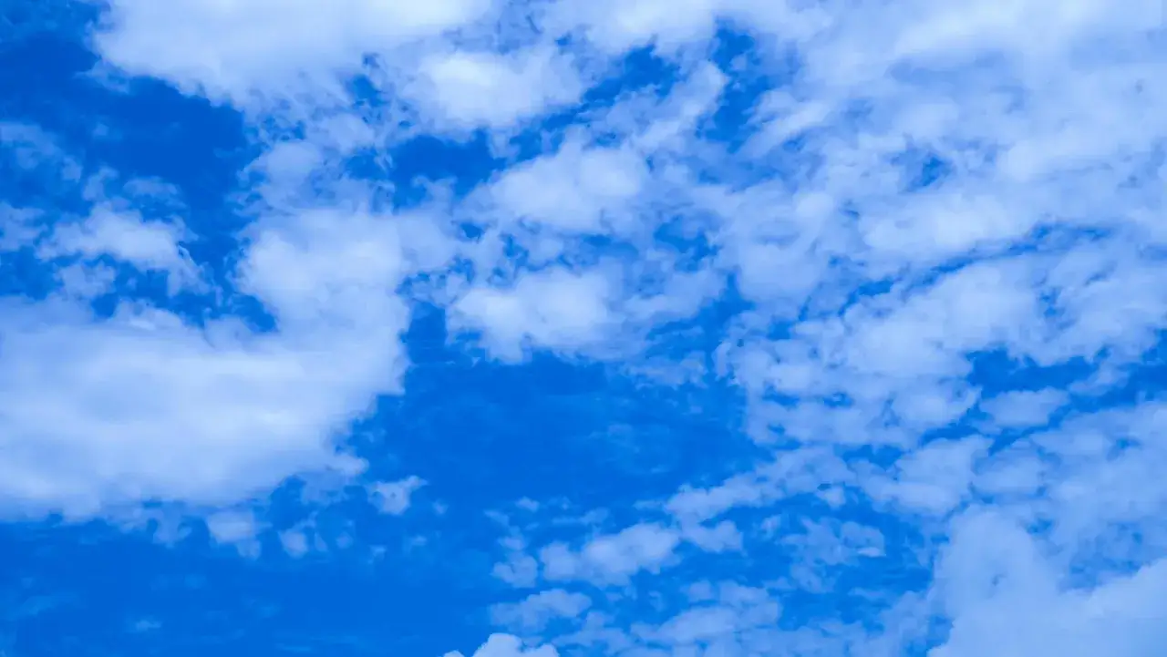 Vaste ciel bleu parsemé de nuages blancs cotonneux, évoquant une journée d'été paisible.