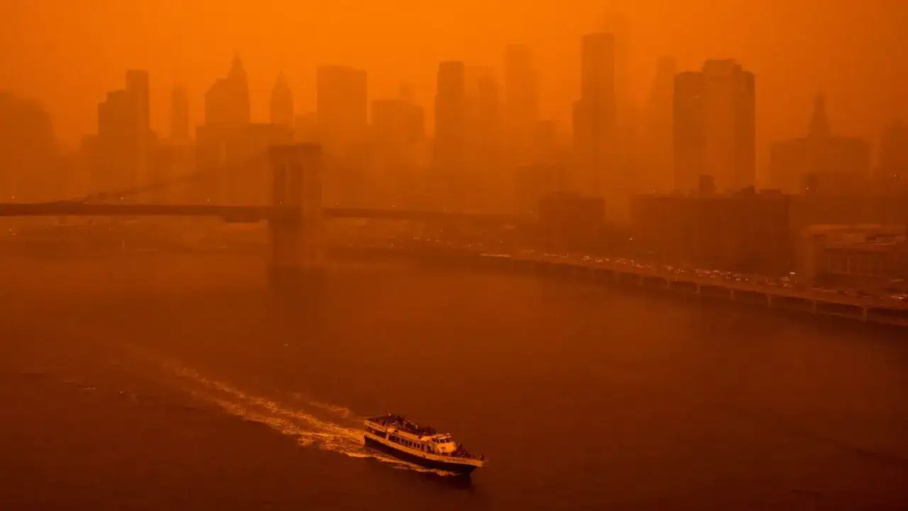 Un ciel orange enveloppe New York, avec le pont de Brooklyn et des gratte-ciel fantomatiques. Un bateau navigue sur l'eau, comme pour chercher pourquoi le ciel est orange.