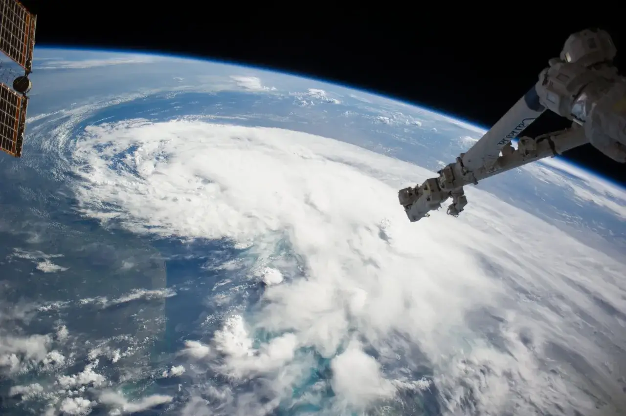 Vue de la Terre depuis l'espace, avec un ouragan massif. Le bras robotique de la Station Spatiale Internationale est visible. La courbure de la Terre est évidente, contredisant l'idée de la terre plate.