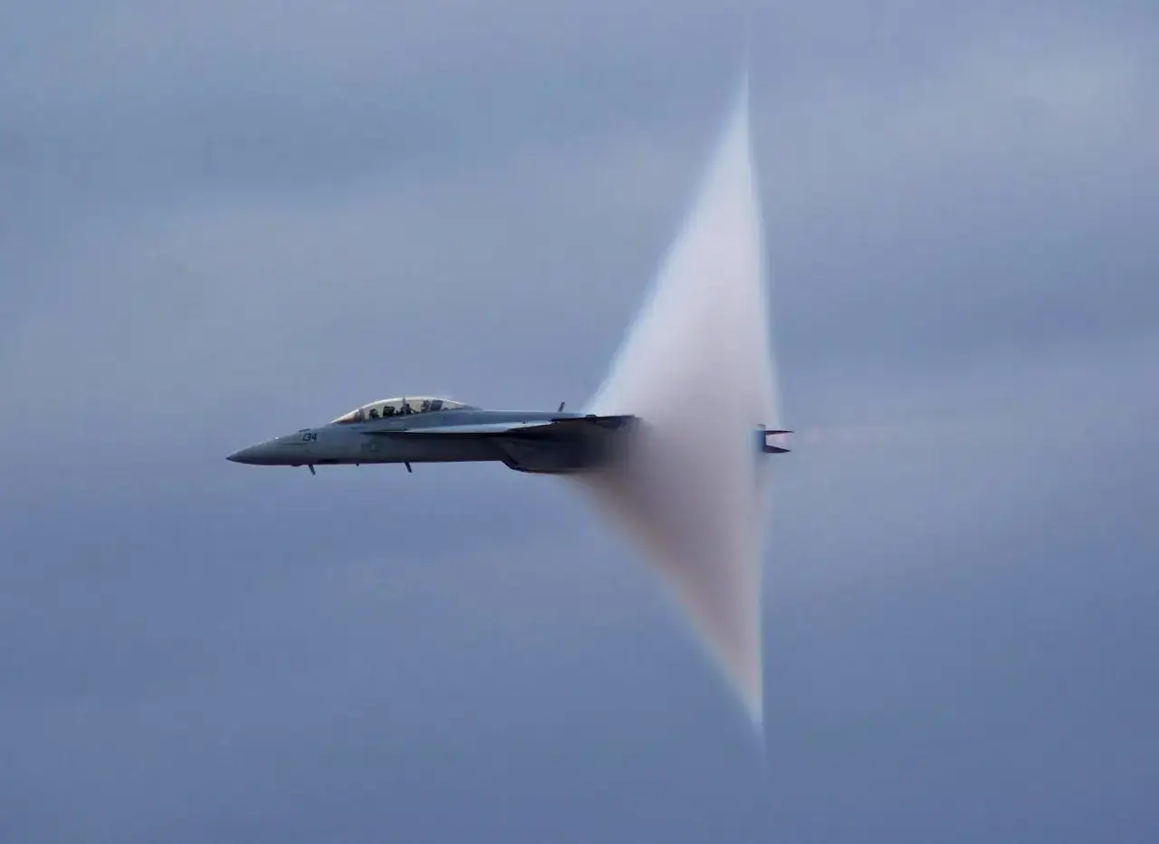 Un avion de chasse crée un cône de condensation spectaculaire, témoignant de la vitesse supersonique.