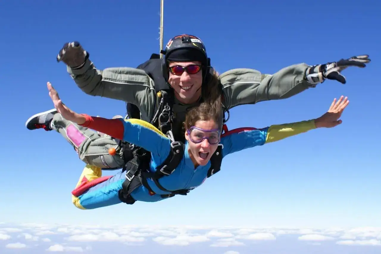 Deux parachutistes en tandem profitent de la vitesse d'un saut en parachute, bras écartés, au-dessus des nuages.
