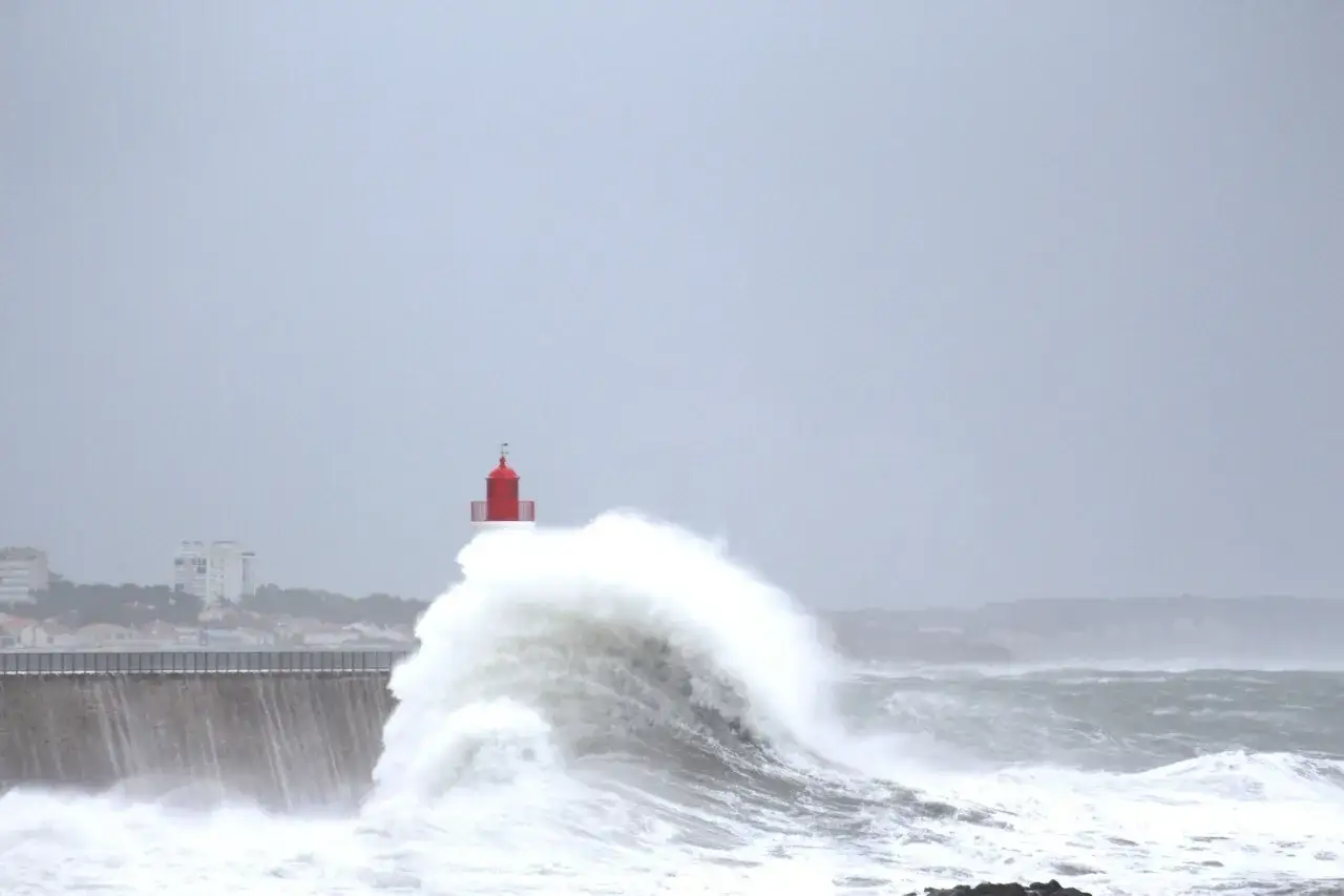 Un phare rouge se dresse au milieu d'une vague déferlante, témoignant d'un puissant coup de vent sur la côte.